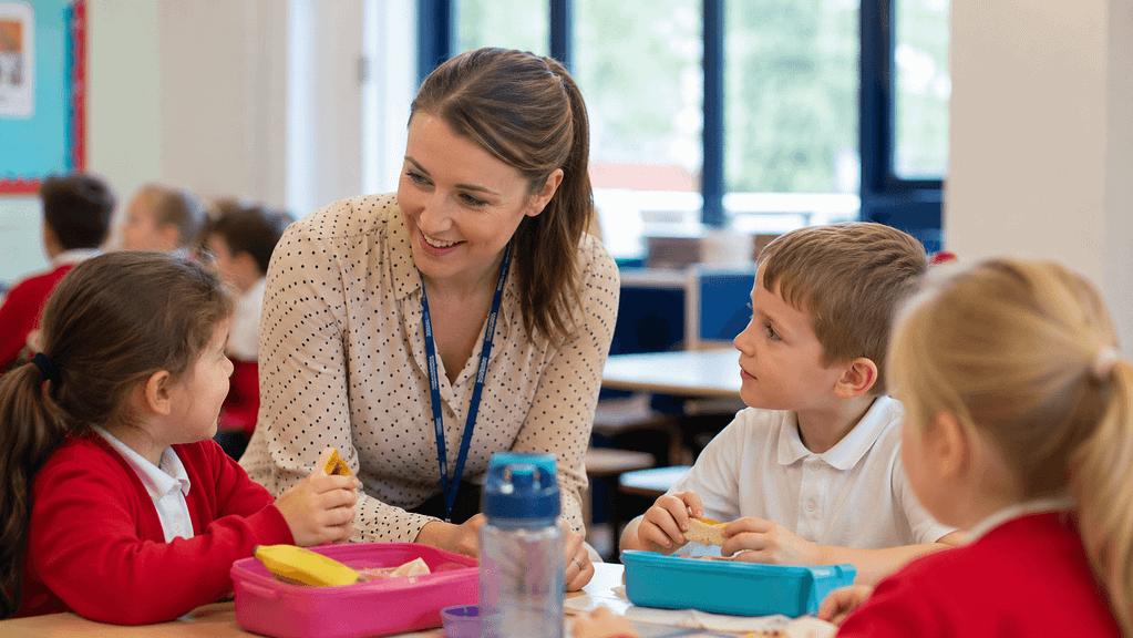 Teacher supervising pupils during lunchtime in a primary school classroom