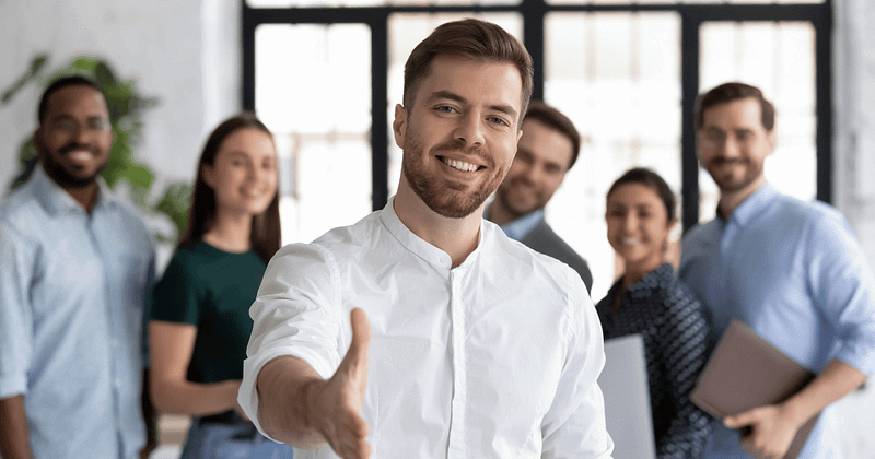 man offering a handshake with four blurred our business people in the background