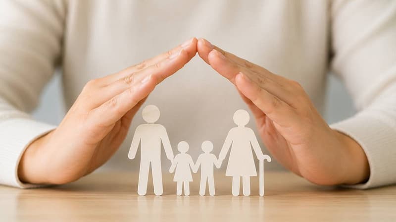 Conceptual image of protective hands sheltering adult, child and older person figures to represent safeguarding and protection.